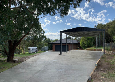 Concrete driveway with a carport surrounded by greenery.