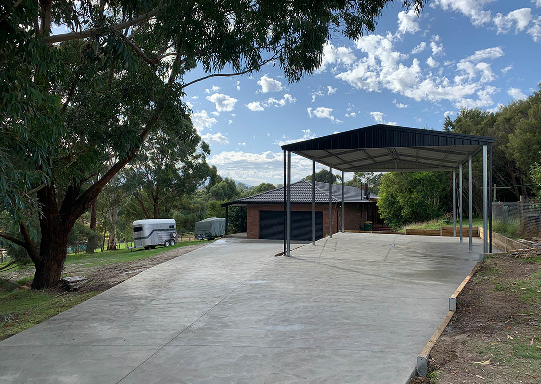 Concrete driveway with a carport surrounded by greenery.
