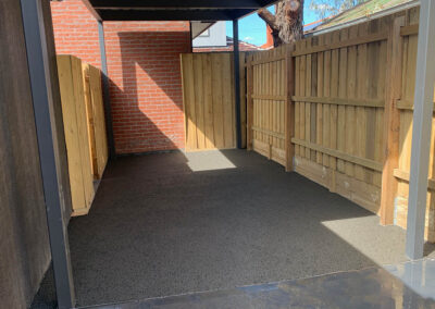 Permeable concrete surface under a covered area, surrounded by wooden fencing.