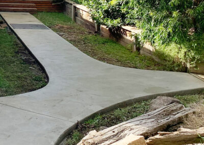 Curved concrete pathway around a house with surrounding greenery.