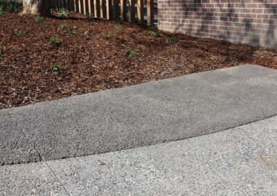 Permeable concrete pathway adjacent to a mulched garden bed near a brick wall.