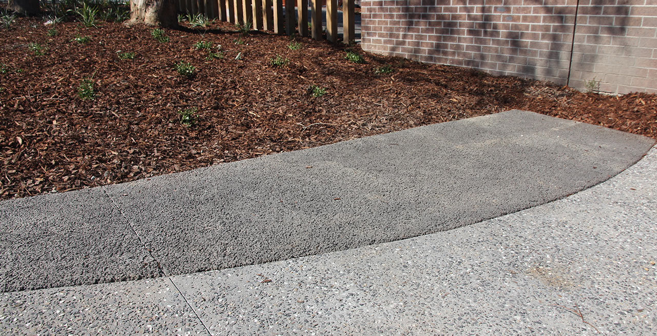 Permeable concrete pathway adjacent to a mulched garden bed near a brick wall.