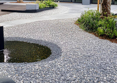 Modern landscaped area with gravel, small pond, and lush greenery.