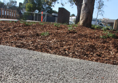 Permeable concrete pathway next to a mulched garden area with a tree.