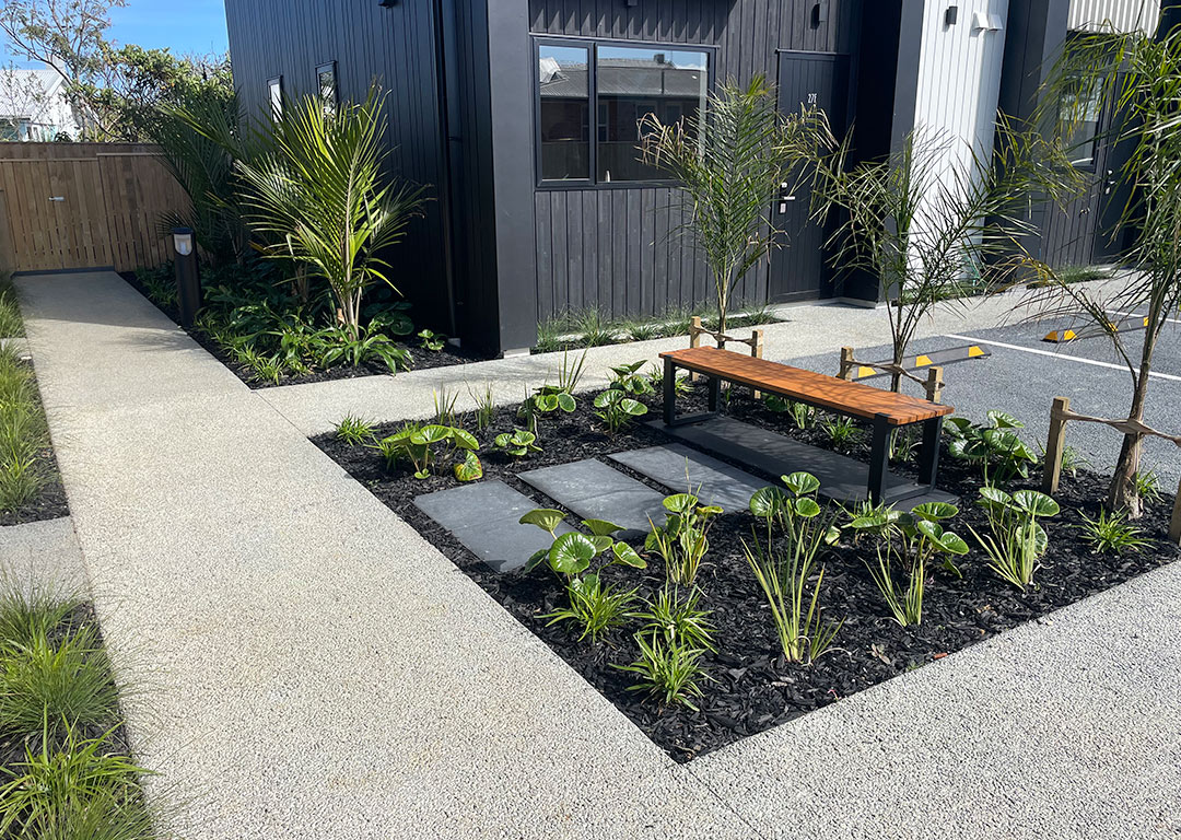Curved concrete pathway around a house with surrounding greenery.
