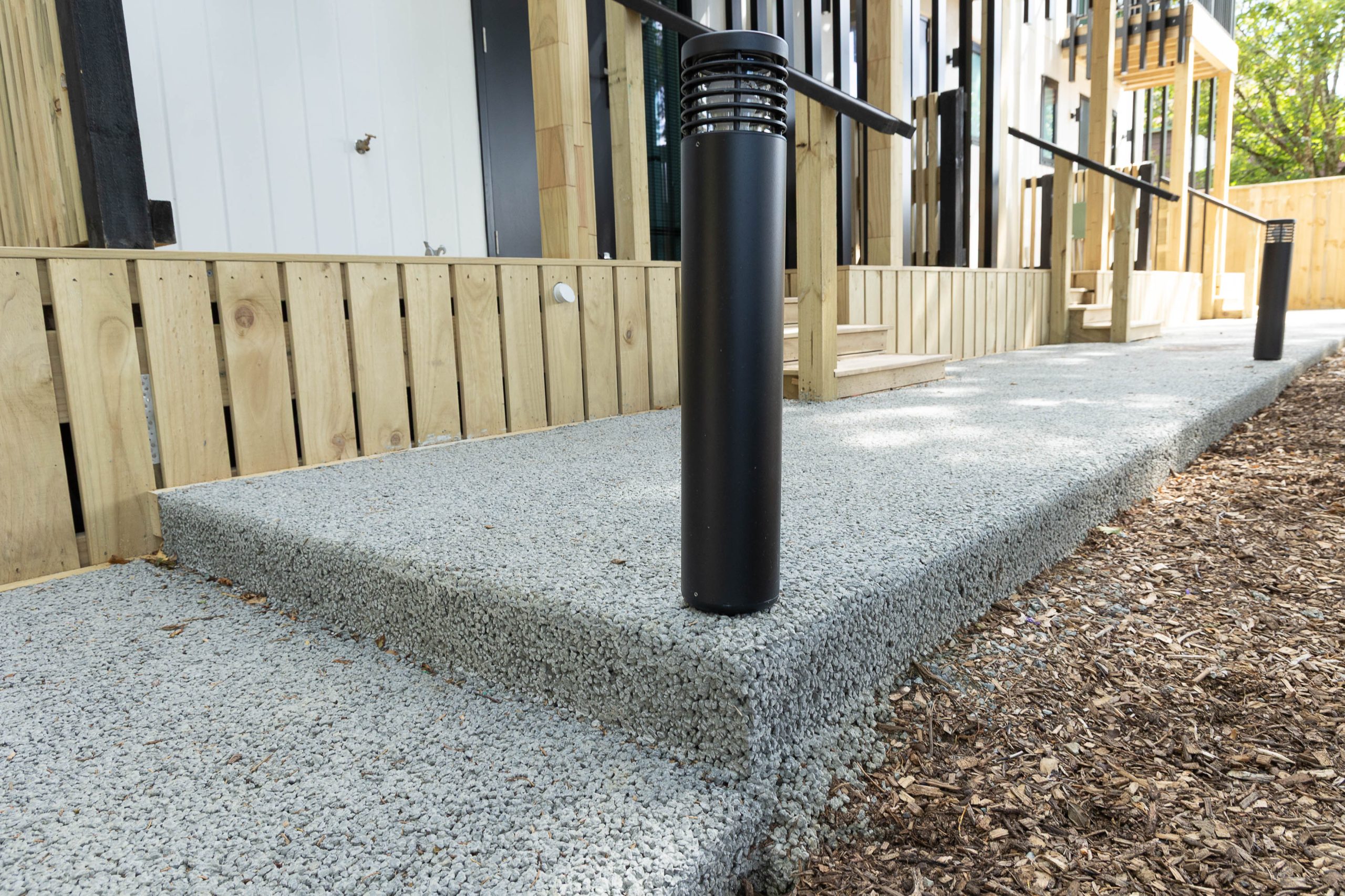 Small landscaped area with permeable concrete surface next to a garden bed and brick wall.